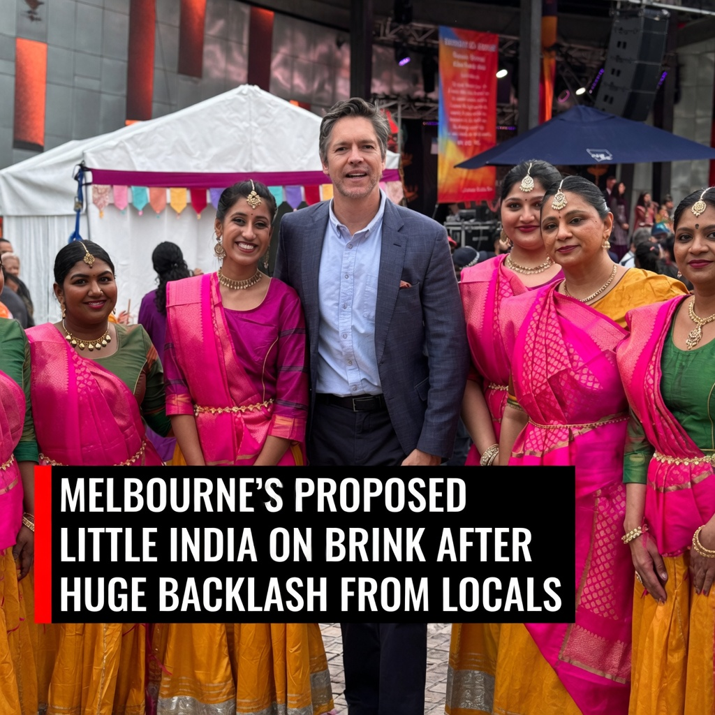 A male politician standing in a gray blazer surrounded by South Asian female dancers in pink and yellow saris