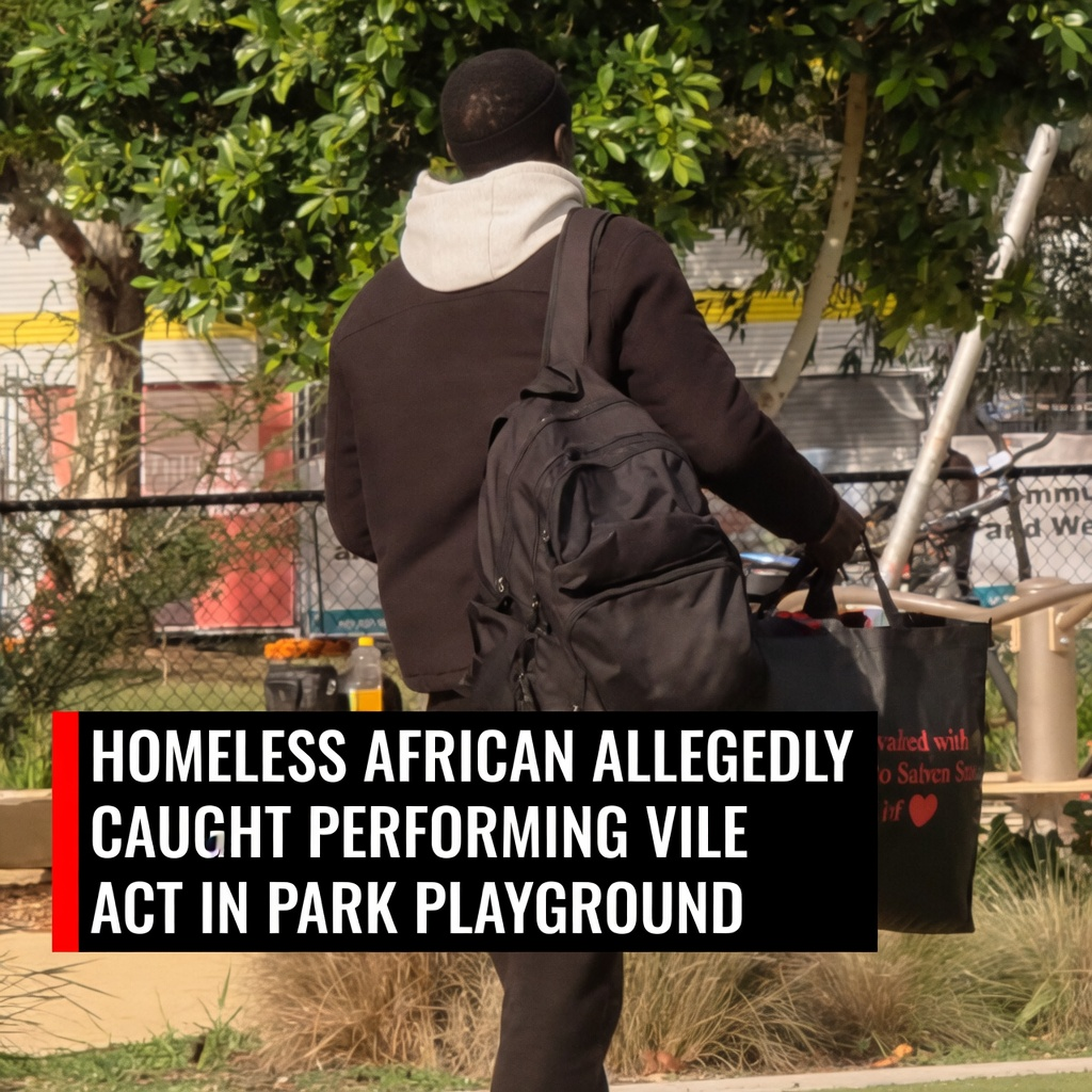 Homeless African vagrant carrying a black backpack walking away from a public children playground corridor